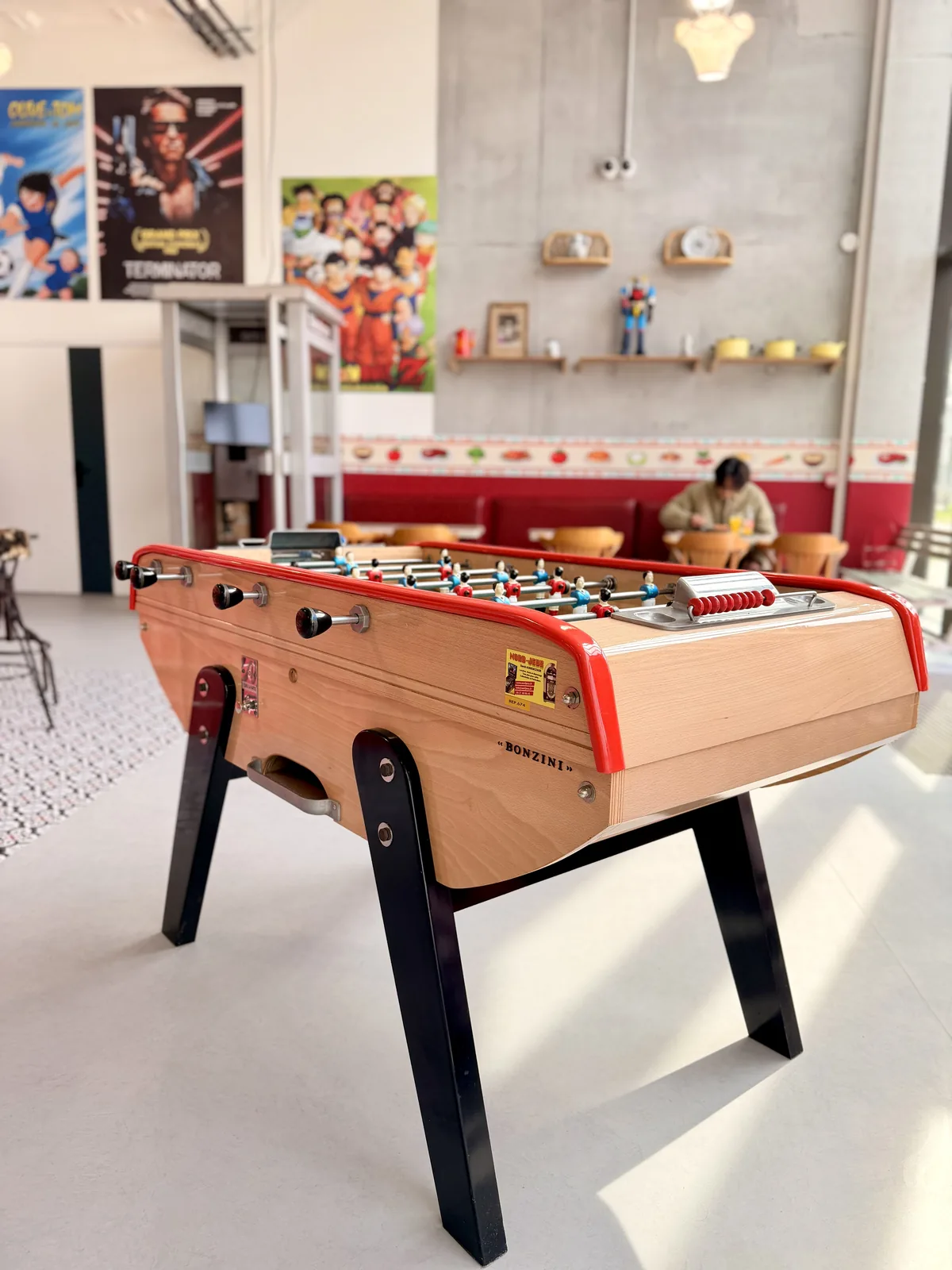 Baby-foot, banquettes rouges et affiches Dragon Ball, Olive et Tom